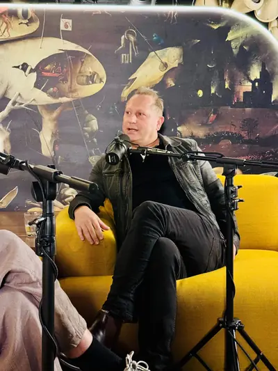 Podcast guest seated in front of a Bosch-style mural in a yellow-lit studio