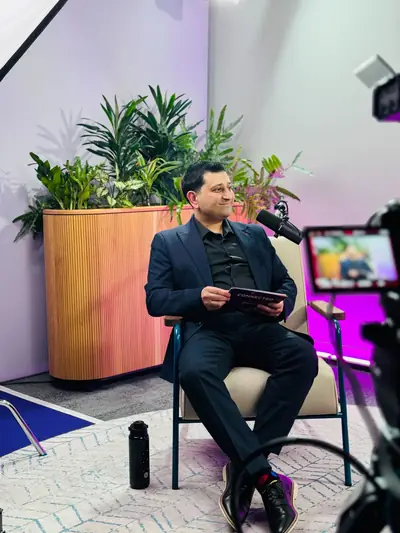 Suited host presenting a podcast in a purple-lit studio