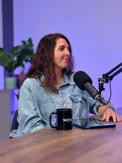 Guest in a denim jacket recording a podcast under purple studio lighting