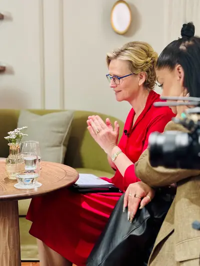 Guest in a red dress being interviewed on a lounge-style podcast set