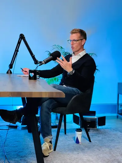 Guest in a blue cardigan speaking into a microphone during a studio podcast recording